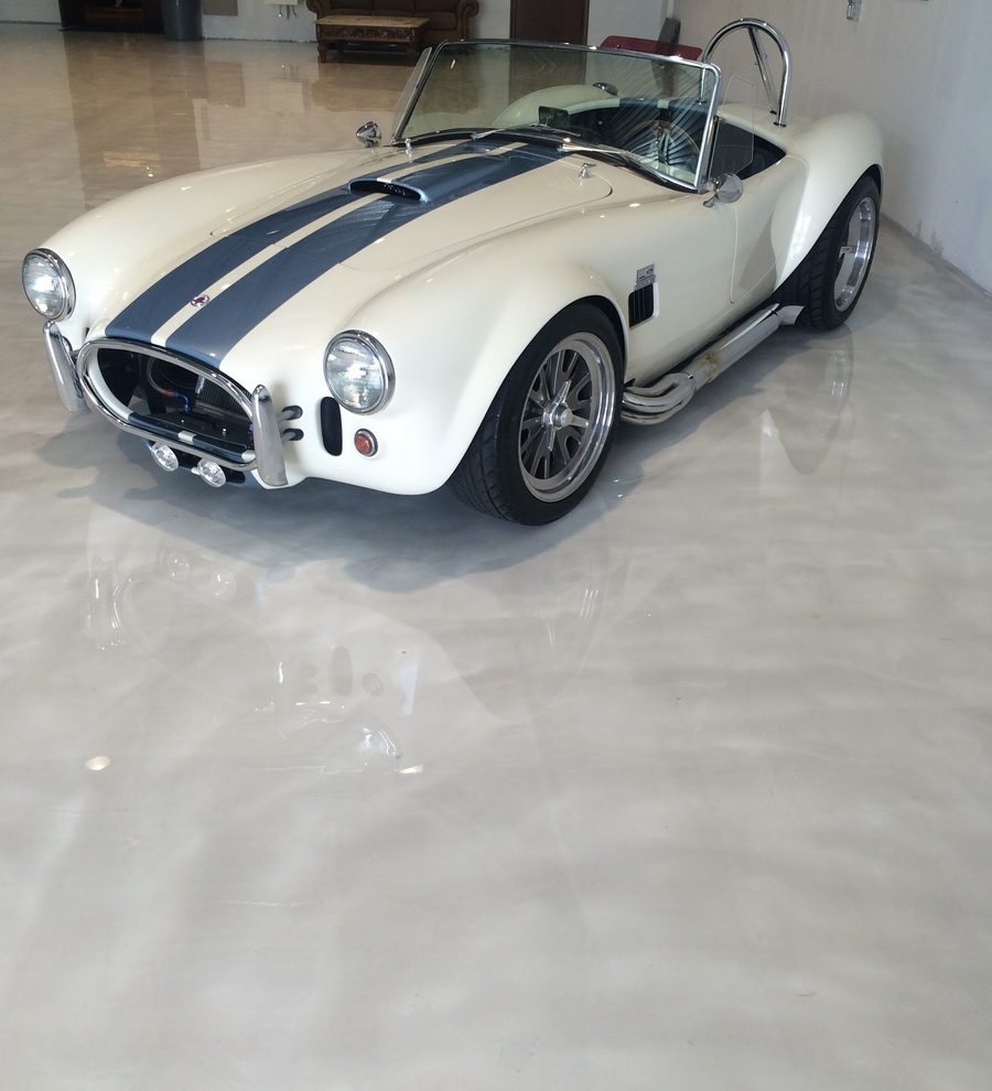 White classic roadster with blue stripes parked on a pale silver metallic epoxy floor