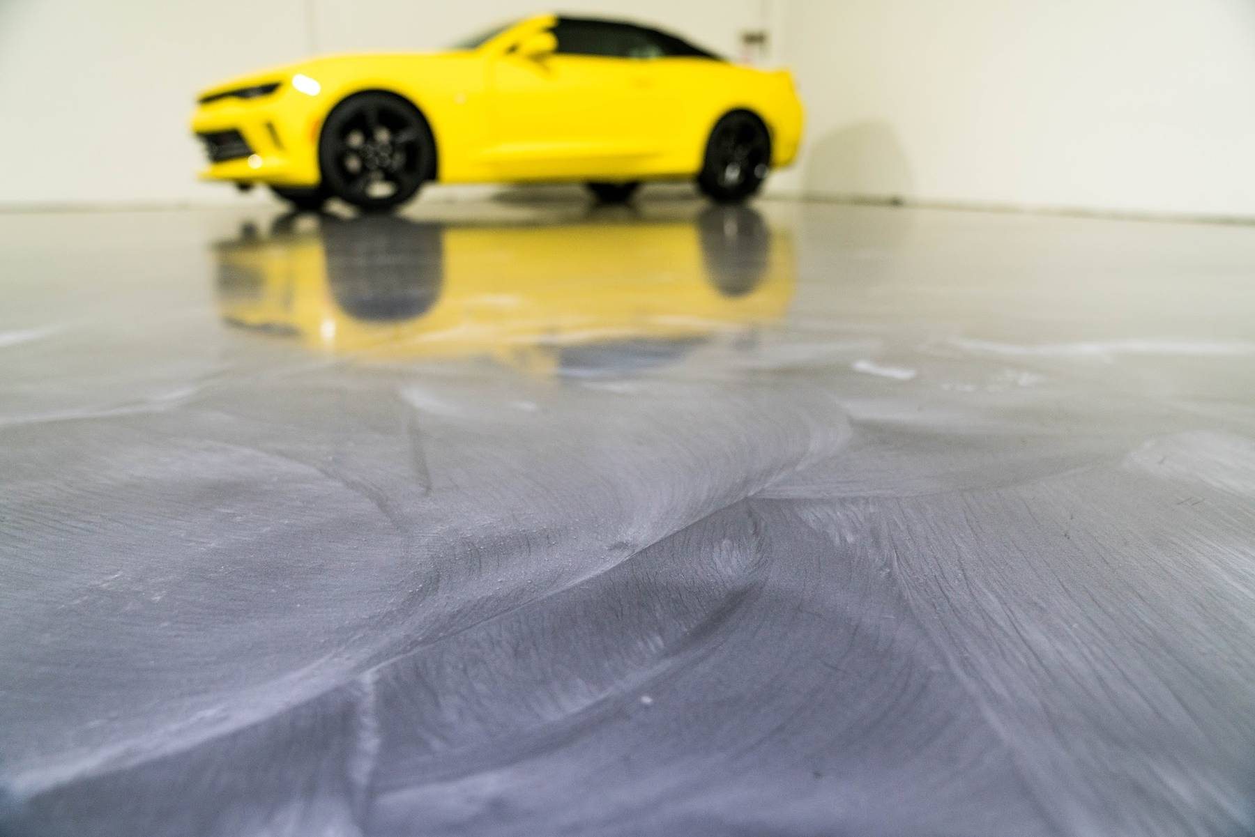 Silver and gray metallic epoxy floor reflecting a yellow sports car